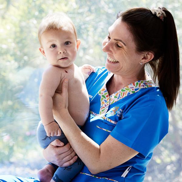 A woman in blue scrubs gently holds a baby, showcasing a caring and professional demeanor in a healthcare setting.